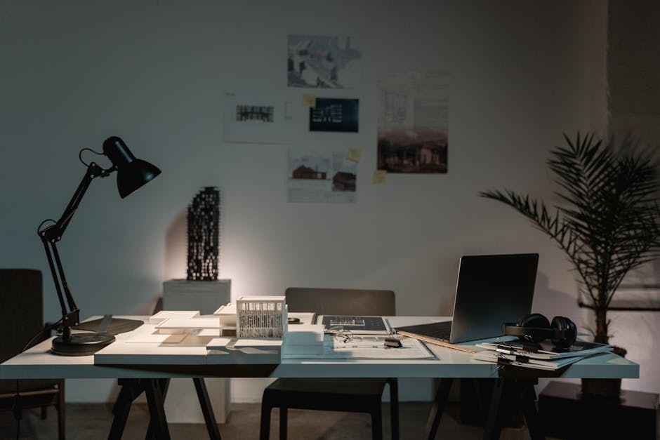A contemporary architect's desk with design plans, laptop, and lamp in a spacious office.